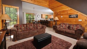 Una sala de estar acogedora con dos sofás de cuero marrón, un reposapiés negro y techo de madera.