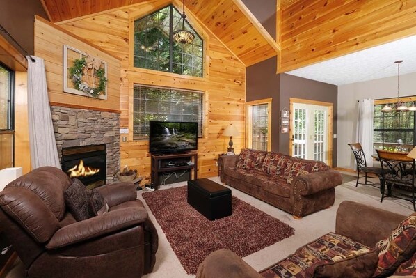 A cozy living room with a stone fireplace, wooden walls, a large TV, and comfortable seating.