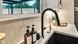 A modern kitchen with a black sink, a window with a view of greenery, and two hand soap bottles on the counter. - Lonetree Ranch an Outdoor Oasis w/ hot tub near Baylor/Magnolia (Waco)