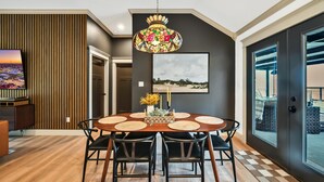 A dining area with a round table, black chairs, a stained glass pendant light, and a cityscape painting on the wall. - Lonetree Ranch an Outdoor Oasis w/ hot tub near Baylor/Magnolia (Waco)