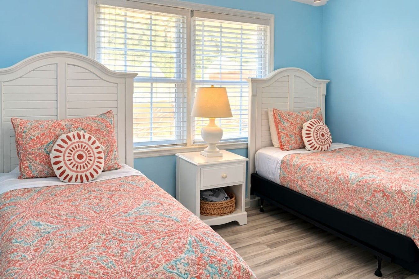 A bedroom with two beds, a nightstand, a lamp, and a window with blinds.