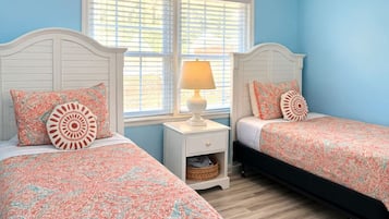 A bedroom with two beds, a nightstand, a lamp, and a window with blinds.