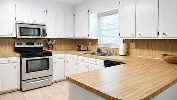 A modern kitchen with white cabinets, stainless steel appliances, a wooden countertop, and a window with blinds.