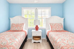 A bedroom with two beds, a nightstand with a lamp, and a window with blinds.