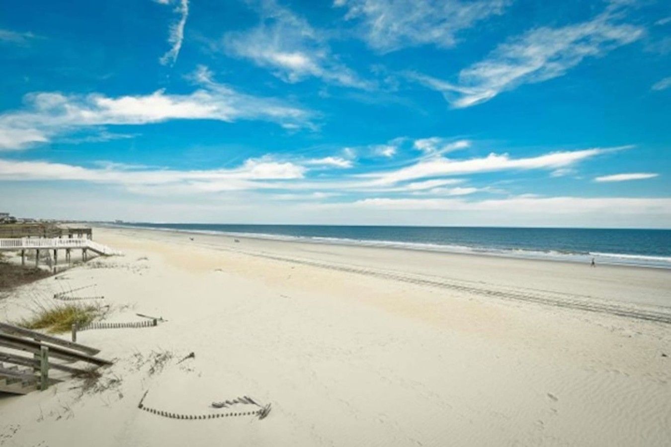 Una playa con un muelle de madera y cielo despejado.