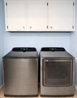 Two front-loading stainless steel dryers side by side against a light blue wall, with a white cabinet above.