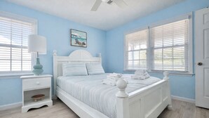 A bedroom with a bed, nightstand, lamp, and windows with blinds. - Easy Like Sunday ★ Pet-Friendly ★ Walk to Beach ★ Sleeps 10 (Murrells Inlet)