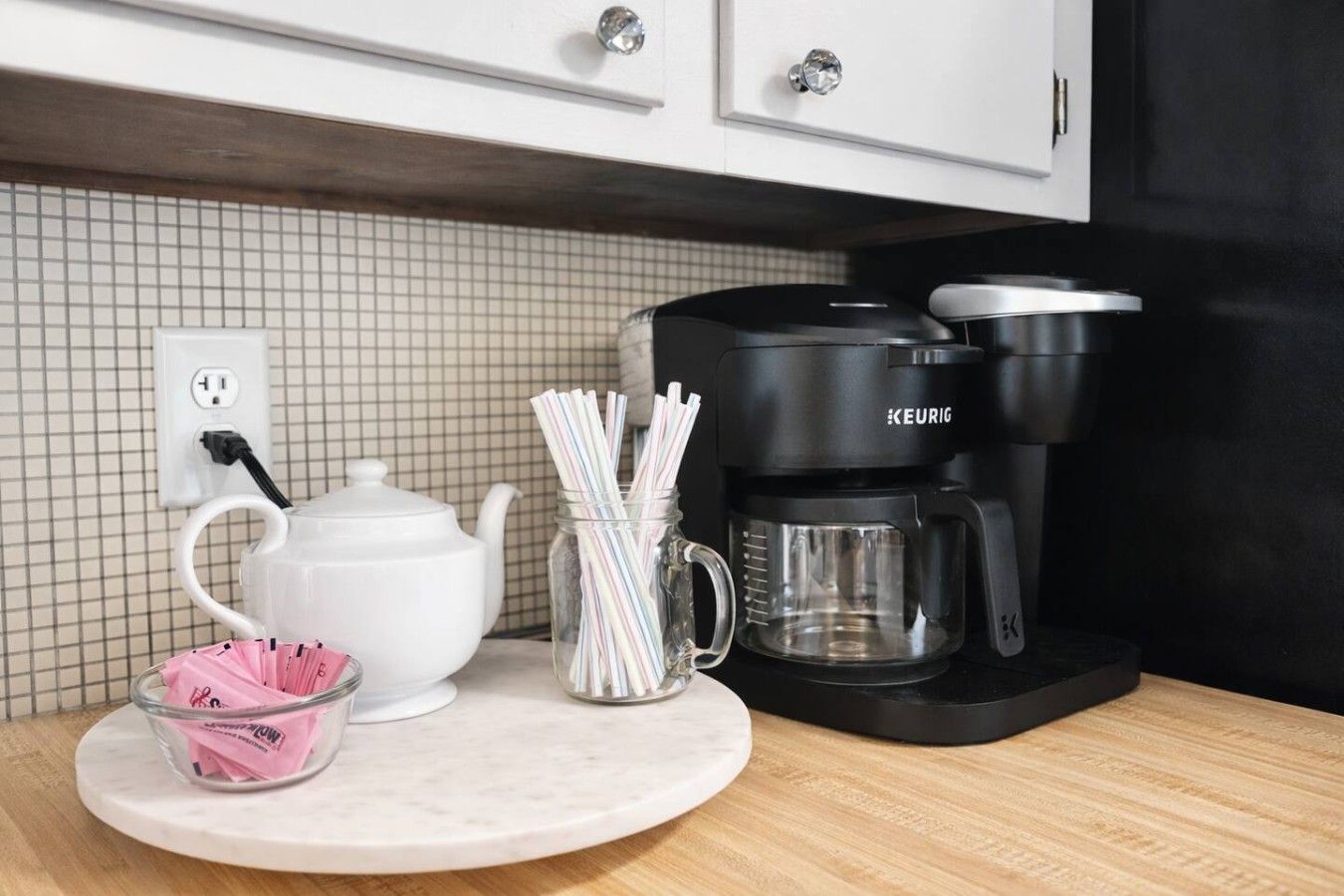 A kitchen counter with a white teapot, a coffee maker, and a glass jar with straws.