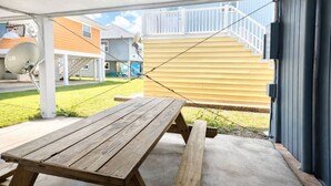A covered patio with a wooden table and benches, a satellite dish, and a staircase leading to a yellow house. - Easy Like Sunday ★ Pet-Friendly ★ Walk to Beach ★ Sleeps 10 (Murrells Inlet)