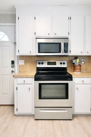 A kitchen with white cabinets, a microwave, a stove, and a wooden countertop.
