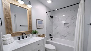 A modern bathroom with a white marble shower, a large mirror, and a white toilet. - Easy Like Sunday ★ Pet-Friendly ★ Walk to Beach ★ Sleeps 10 (Murrells Inlet)