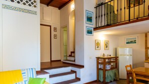 Un intérieur chaleureux avec un escalier menant à un balcon, un coin repas avec une table et des chaises, et une cuisine équipée d’un réfrigérateur.