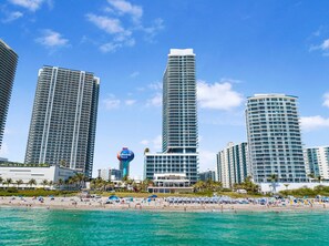 A beachfront hotel with high-rise buildings, a beach, and a clear blue sky.