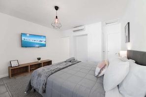 Een moderne slaapkamer met een bed, een televisie, een hanglamp en een deur.