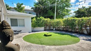 A courtyard with a statue, a small lawn, and a building with a window and shuttered door. - Modern Studio | Perfect Location | Total Comfort (Miami)