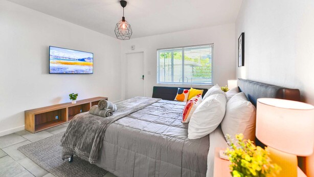 A modern bedroom with a bed, bedside table, lamp, and a painting on the wall. - Modern Studio | Perfect Location | Total Comfort (Miami)