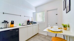 A compact kitchen with a dishwasher, a microwave, and a coffee maker. There is a dining table with a chair and a small potted plant. - Modern Studio | Perfect Location | Total Comfort (Miami)