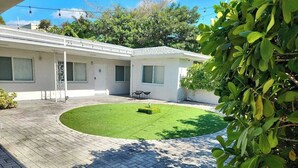 A residential property with a paved courtyard, a small lawn, and a white building with multiple windows and doors. - Miami Studio | Minutes from Design District (Miami)