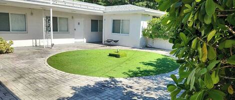 Propiedad residencial con patio empedrado, césped pequeño y un edificio blanco con varias ventanas y puertas.
