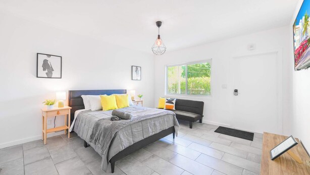 A modern bedroom with a bed, bedside tables, a bench, a window, and a door. - Miami Studio | Minutes from Design District (Miami)