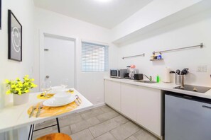 Una cocina compacta con armarios blancos, microondas, cafetera y lavabo. Hay una mesa de comedor preparada con platos, vasos y cubiertos.