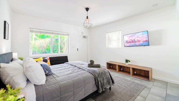 A modern bedroom with a bed, a TV, a window with blinds, and a cityscape view. - Stay Minutes from Miami Hotspots (Miami)