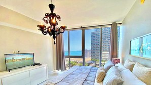 A modern bedroom with a large bed, a television on a white cabinet, and a view of the city and ocean through large windows. - 2BR Bay-View Brickell | Steps to City Centre (Miami)