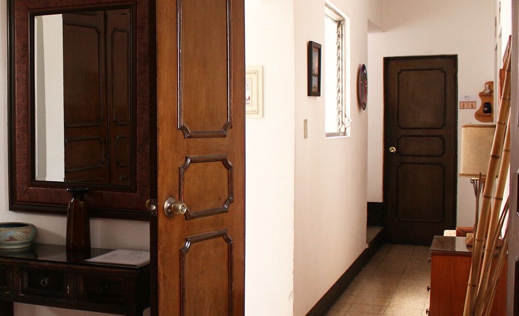 Un pasillo con puerta de madera, un espejo, un cuadro enmarco y una mesita con un cuenco.