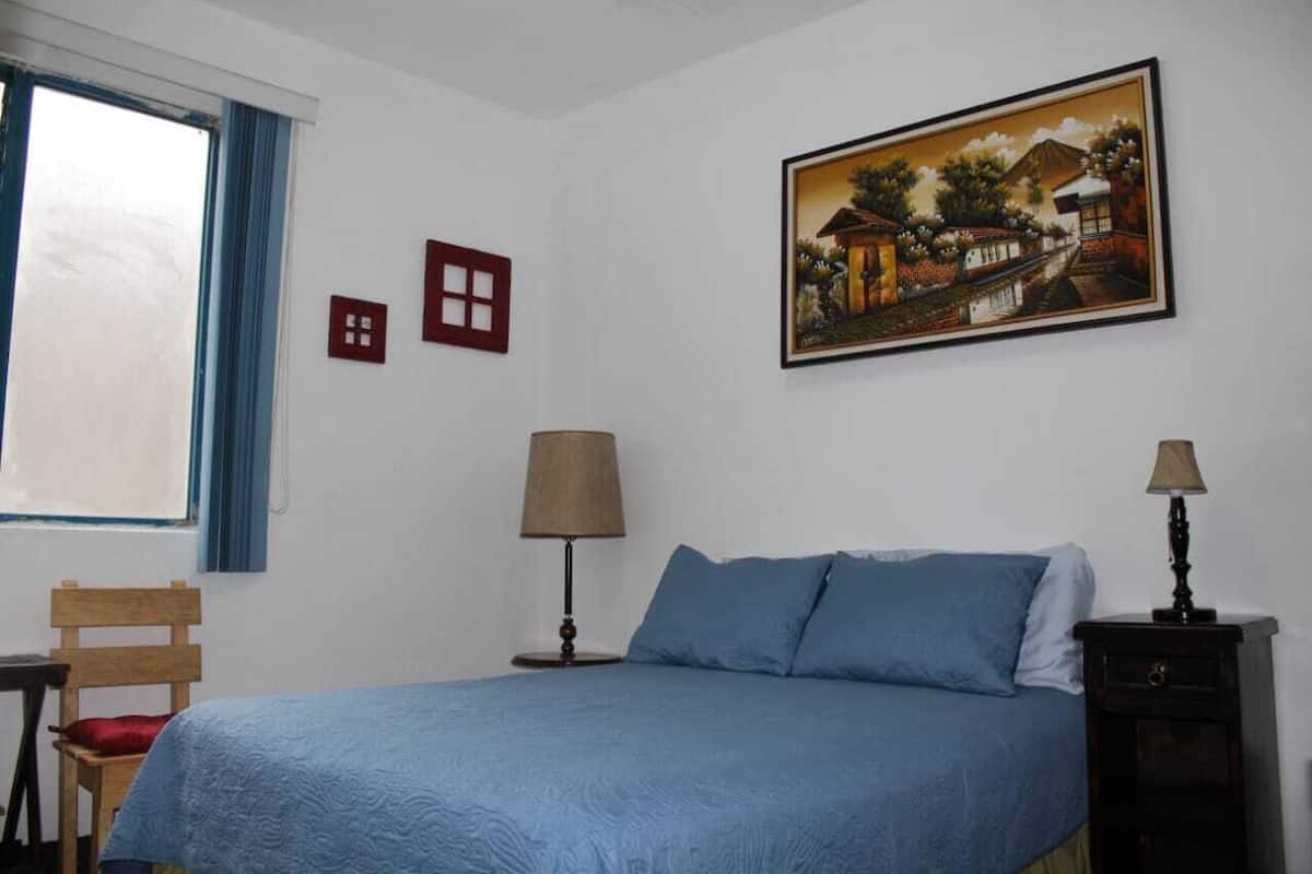 Une chambre à coucher avec un lit, une chaise, une lampe et un tableau au mur.