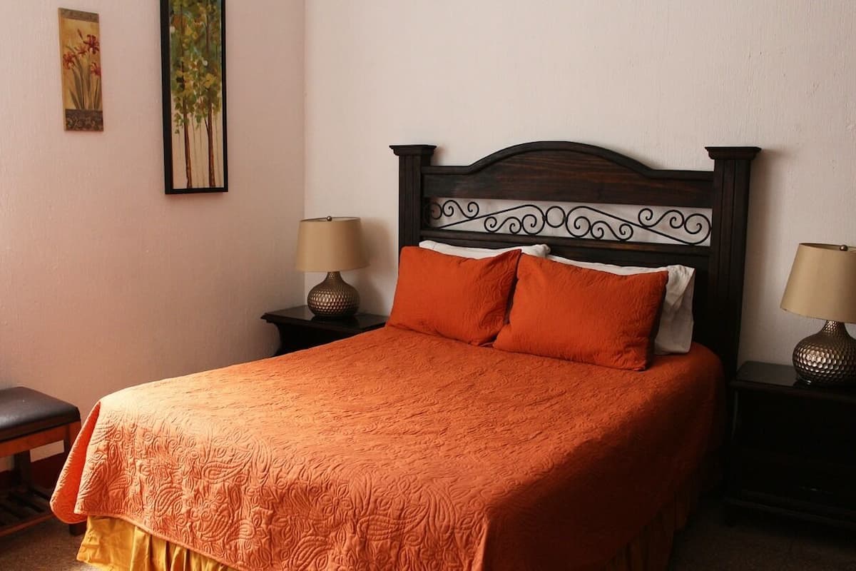 Un lit bien fait, recouvert d’une couvre-lit orange, deux tables de chevet avec des lampes et un banc sur le côté gauche.
