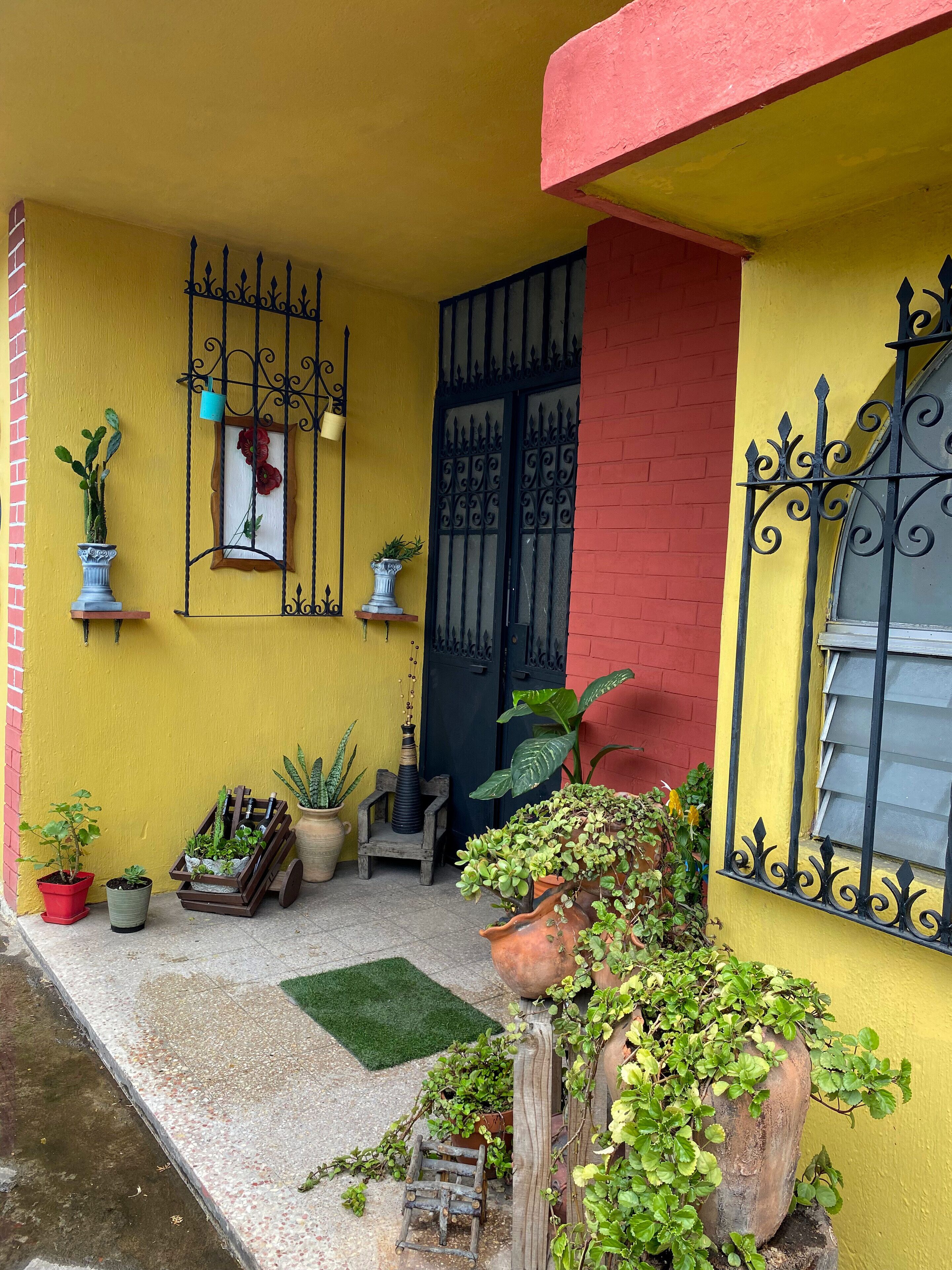 A yellow building with a red door, potted plants, and a small wooden chair outside.