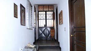 Un pasillo estrecho con una puerta de madera al final, una escalera y una pequeña mesa con un teléfono y una silla.