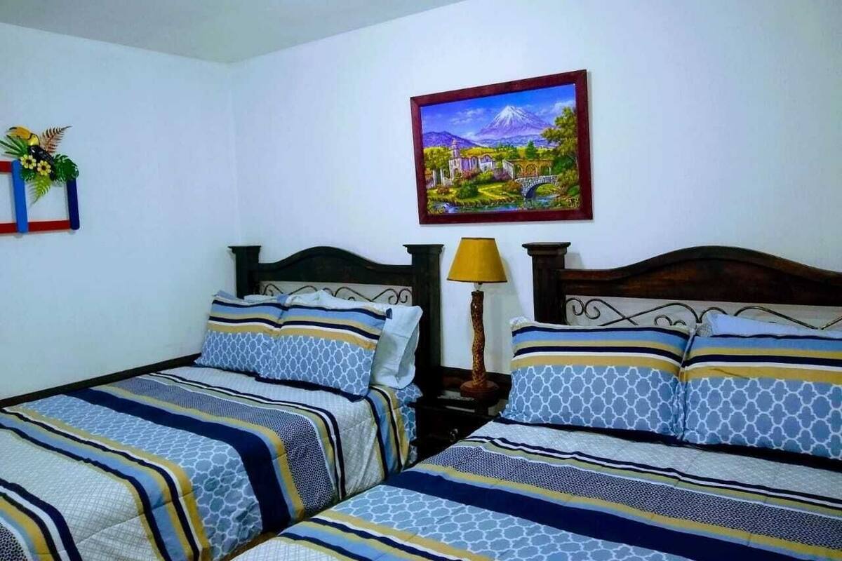Une chambre à coucher avec deux lits, chacun agrémenté de draps à rayures, une table de chevet avec une lampe et un tableau encadré au mur.
