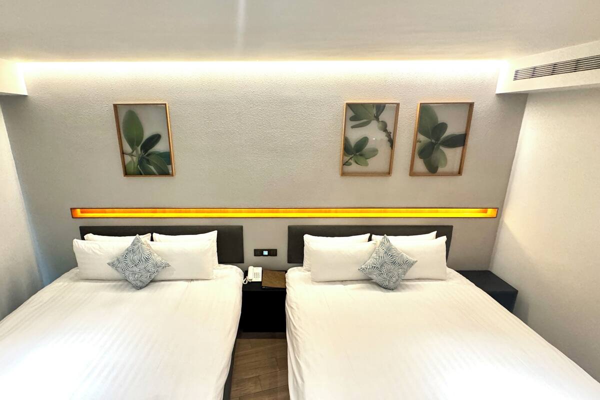 Ett hotellrum med två sängar, ett nattduksbord, en telefon och inramade konstverk på väggen.
