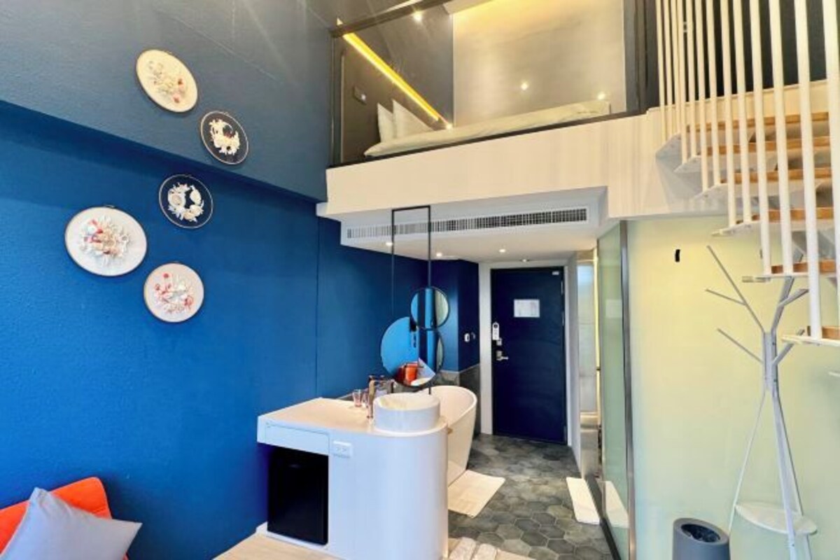 Un moderno vestíbulo de hotel con una pared azul, un mostrador de recepción y una escalera que sube a un nivel superior.