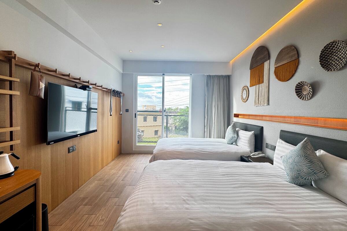 Ett hotellrum med två sängar, en TV, trähyllor och en balkong med utsikt.