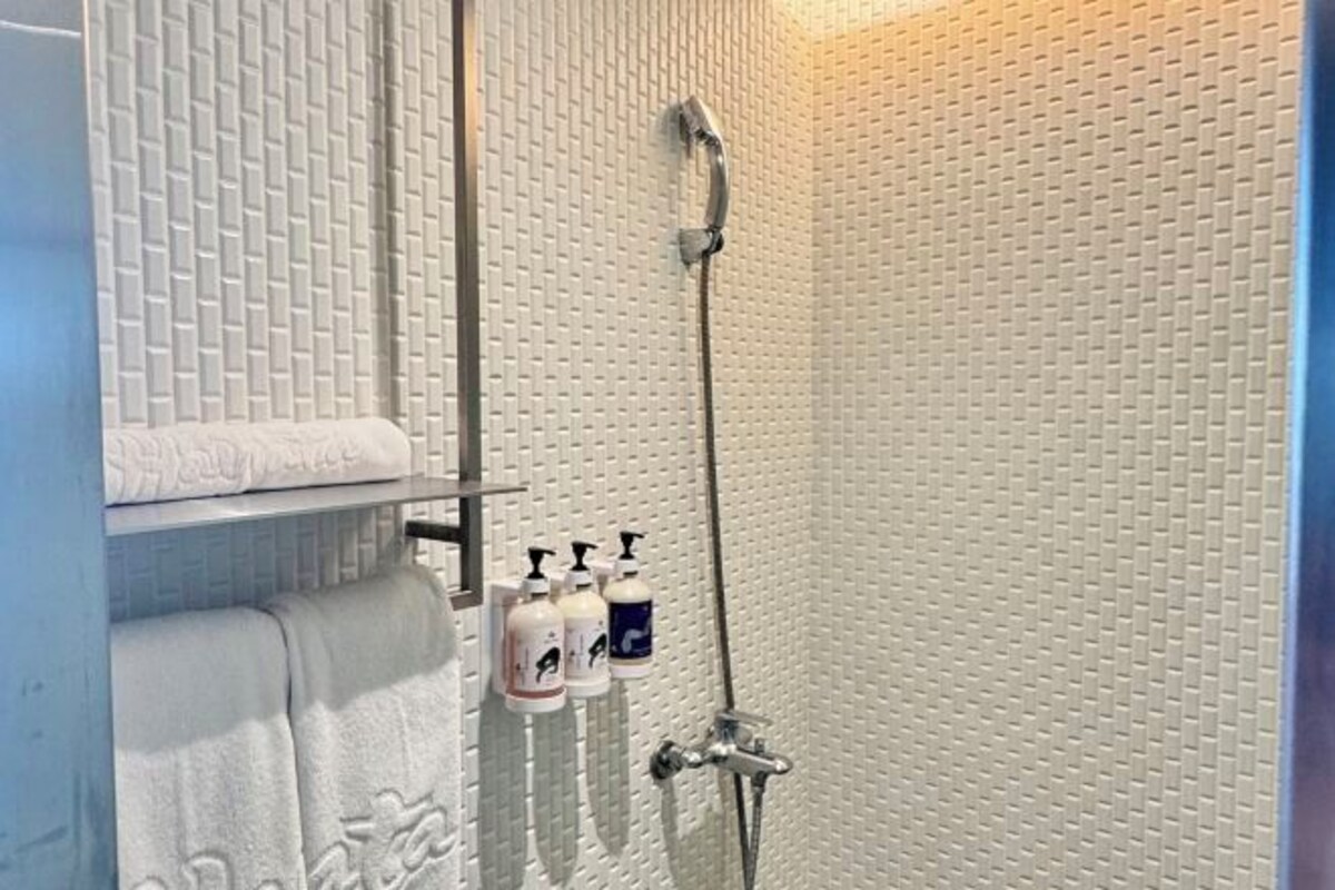 Een badkamer met een structuurwand, een douche met douchehanddouche en een plank met handdoeken en toiletartikelen.