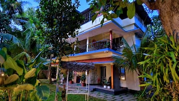 A two-story building with a balcony, surrounded by lush greenery.