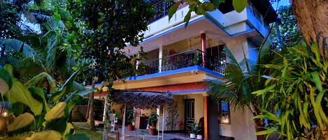 A two-story building with a balcony, surrounded by lush greenery.