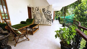 A room with a green sofa, a wooden chair, a small table, and a wall mural. - Aryavilla Heritage (Varkala)