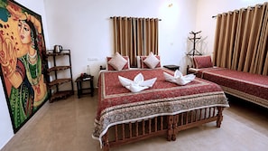 A hotel room with a large bed, a smaller bed, a wooden chair, a nightstand, a lamp, and a painting on the wall. - Aryavilla Heritage (Varkala)