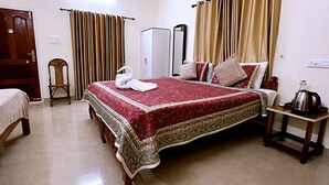 A hotel room with a large bed, a wooden chair, a wardrobe, and a bedside table with a kettle. - Aryavilla Heritage (Varkala)