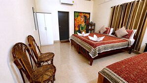 A hotel room with a bed, two wicker chairs, a painting, and a curtain. - Aryavilla Heritage (Varkala)