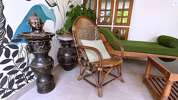 Una habitación con una silla de mimbre, un sofá verde y jarrones decorativos.