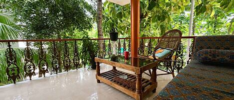 A balcony with a wooden bench, a patterned sofa, and a potted plant.
