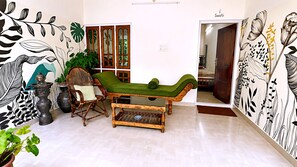 Una habitación con un banco acolchado verde, una silla de madera, una mesita y una pared con motivos florales en blanco y negro.