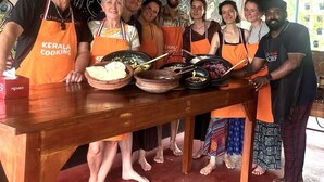 A group of people in orange aprons standing around a wooden table with food items. - Aryavilla Heritage (Varkala)