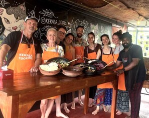 Un grupo de personas con delantales anaranjados de pie alrededor de una mesa de madera con comida.