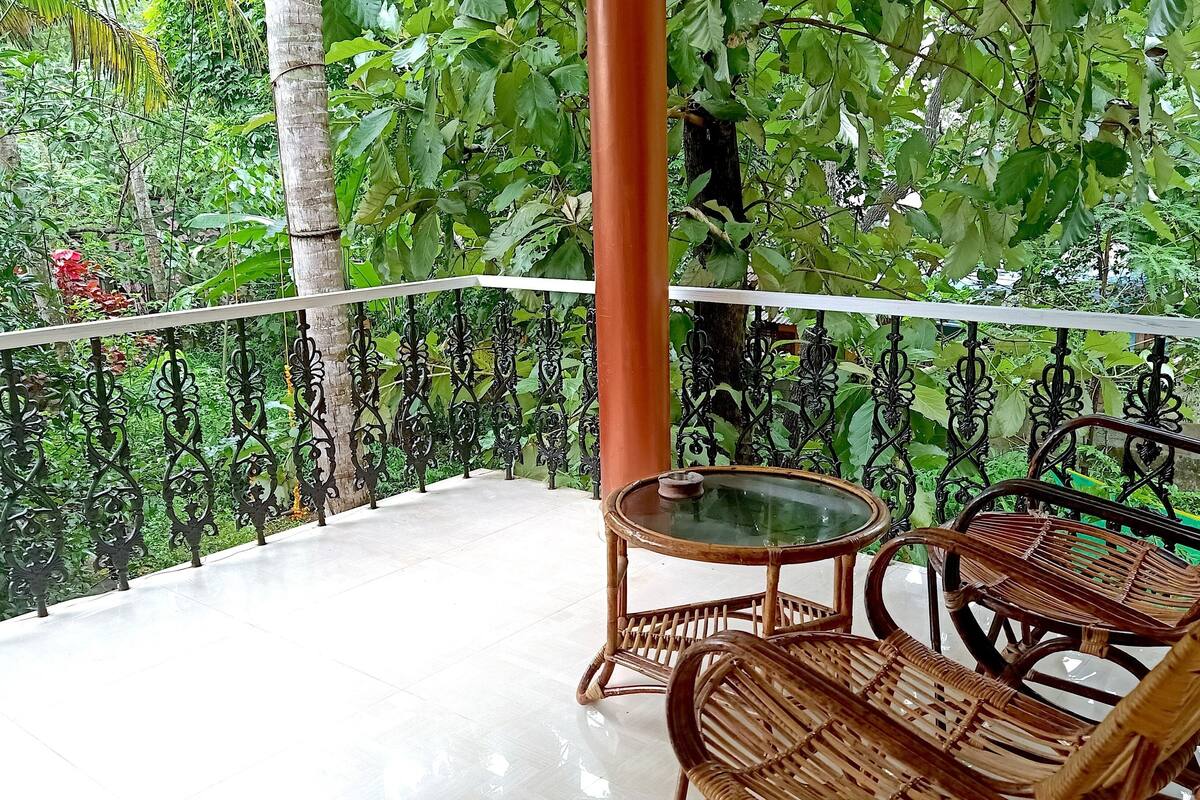 Ein Balkon mit Glastisch und Korbstühlen, umgeben von üppigem Grün.