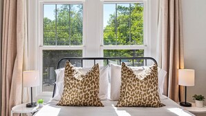 A bedroom with a bed, two windows, curtains, and a nightstand with a lamp.